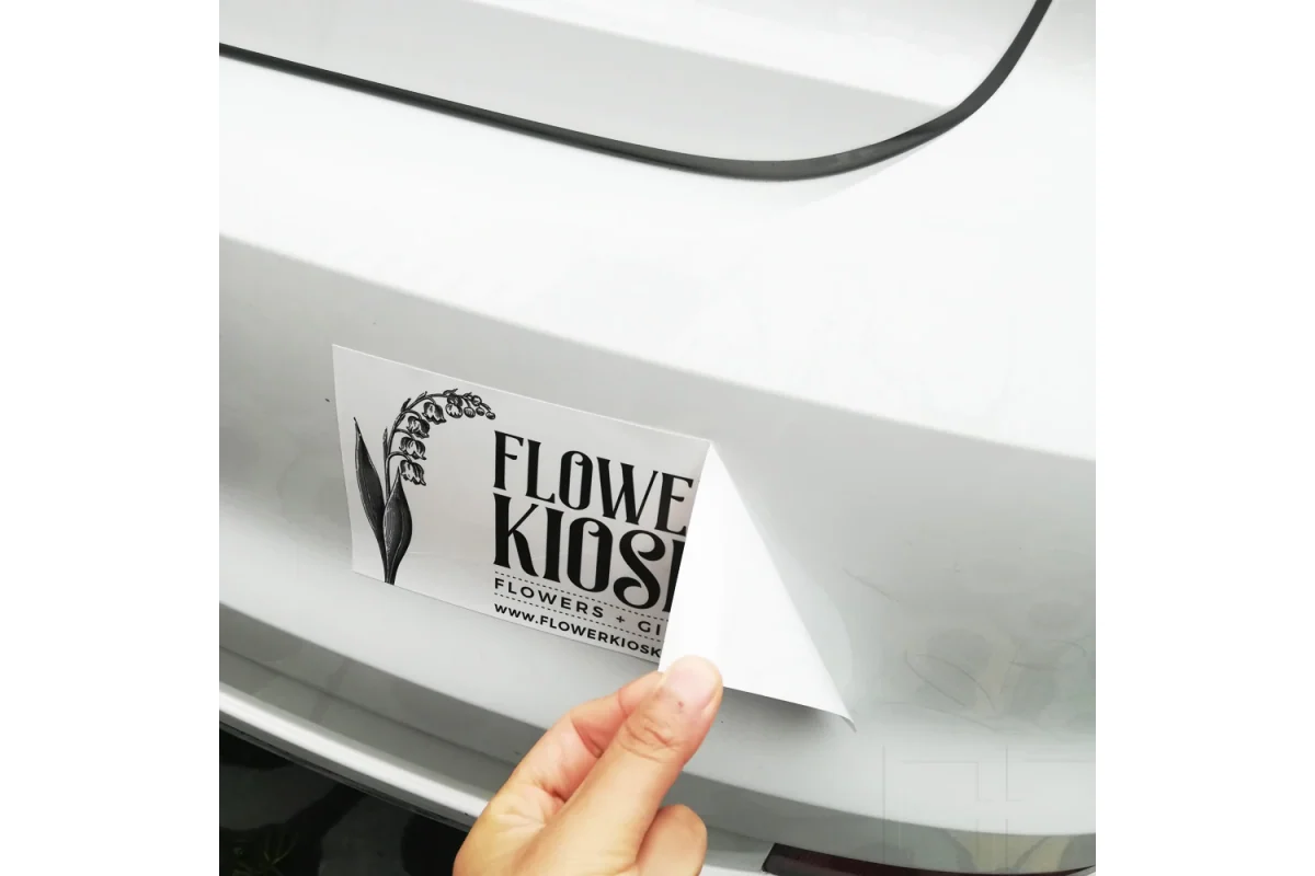 A hand removing backing paper while applying a black lettering decal to a white car panel.