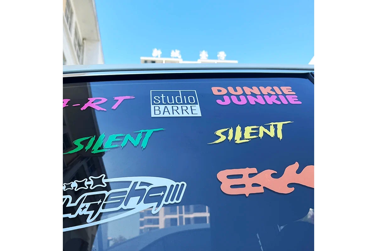 Different colored lettering and logos applied to a dark car window.