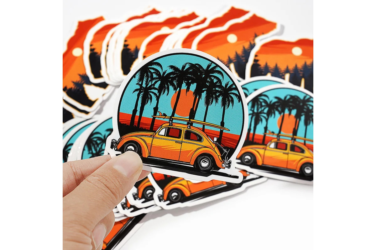 A hand holds a colorful car illustration decal in front of matching printed stickers