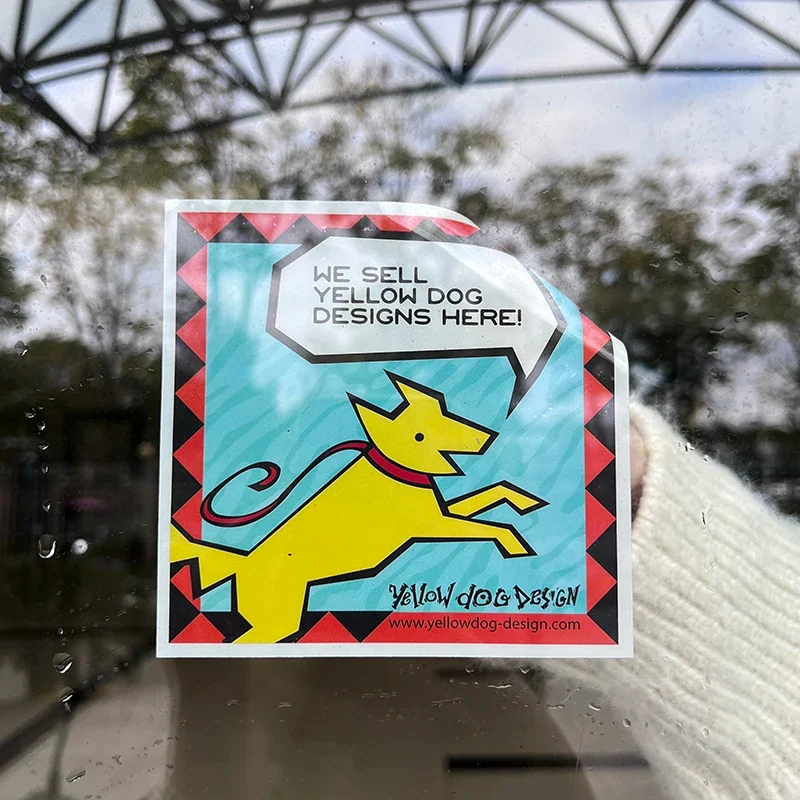 A square full color window decal with a yellow dog illustration on glass.