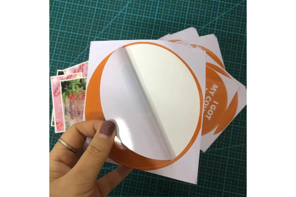 A hand peeling the white backing from a round printed vinyl sticker.