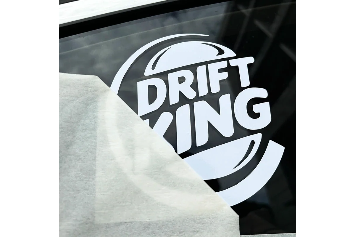 Transfer paper partly lifted from a white lettering decal on dark window glass.