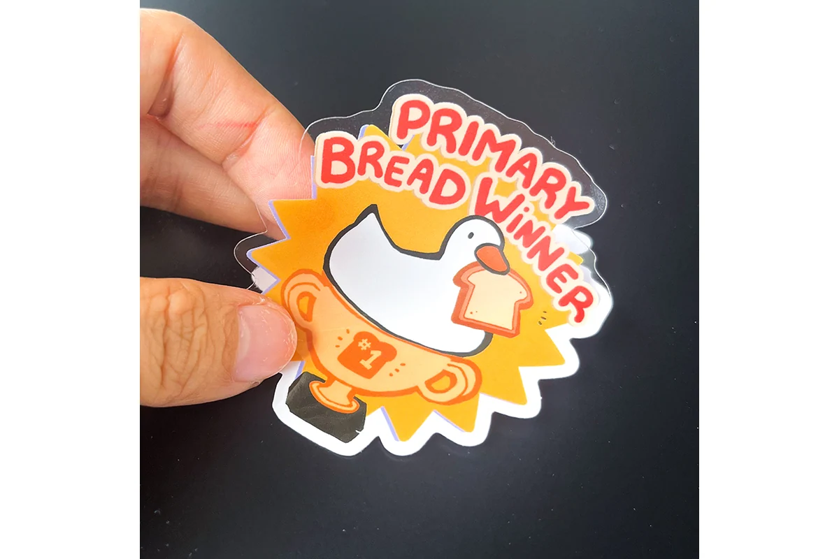 A hand holds a colorful die-cut sticker with a clear film border