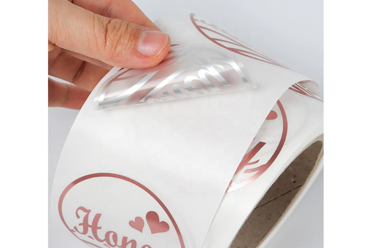 A hand lifts a flexible clear label with red printing from its backing
