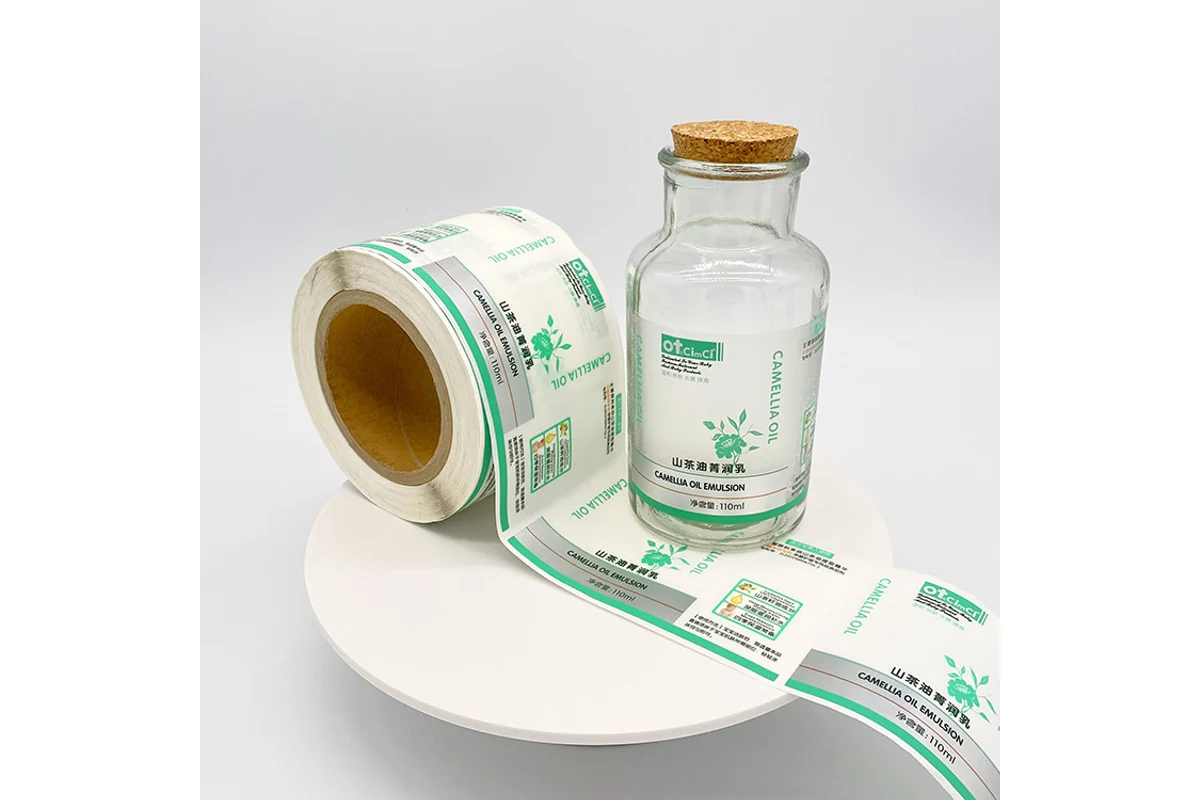 A roll of green printed clear labels beside a labeled glass bottle