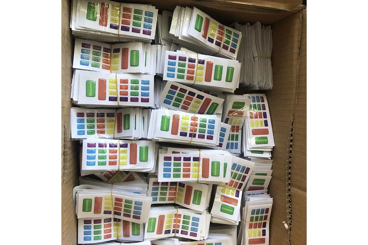 A cardboard box filled with stacks of small colored epoxy sticker sheets.