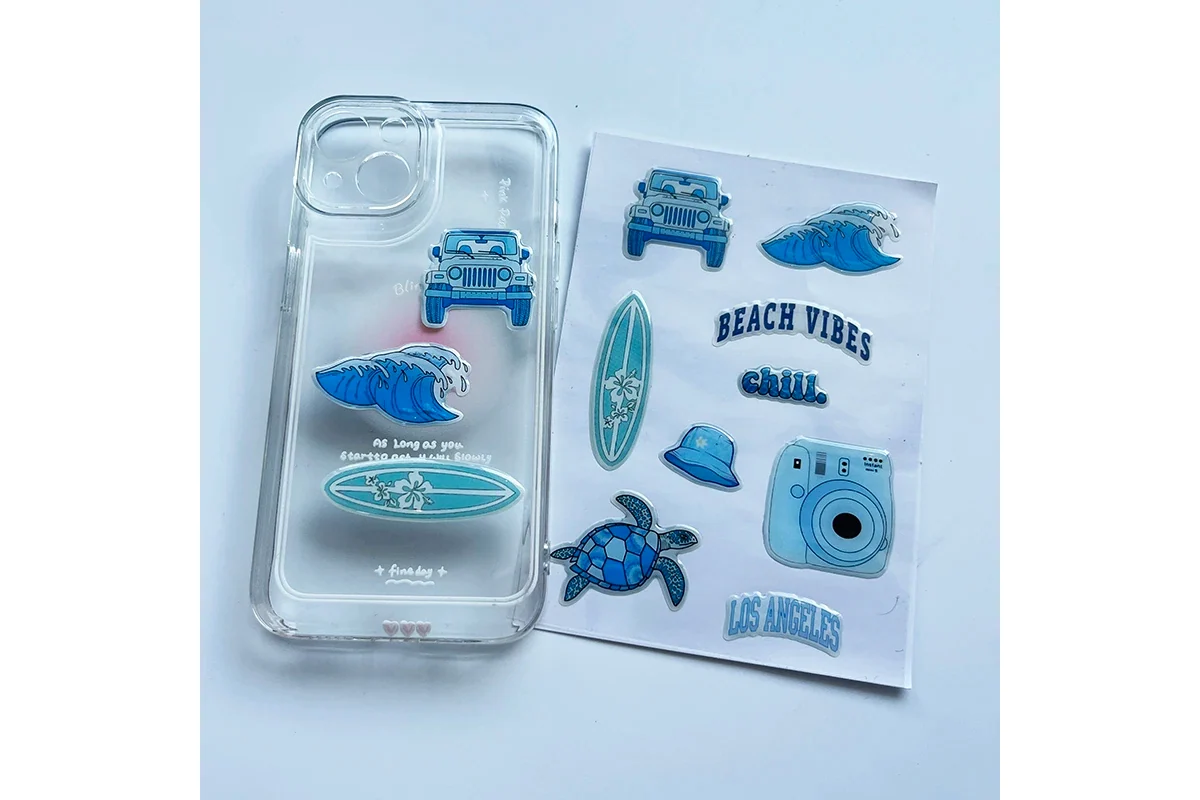 Blue beach themed epoxy stickers shown on a clear phone case beside the sheet.
