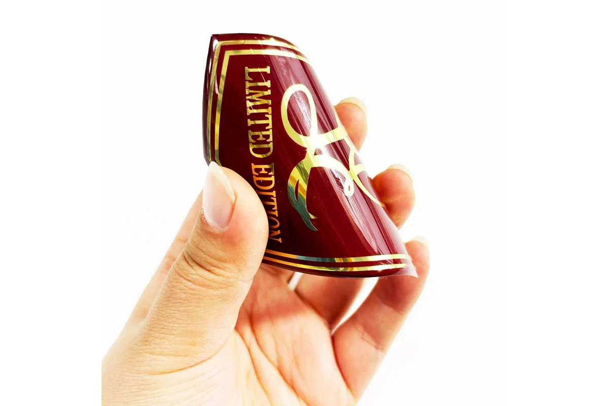 A hand bending a burgundy epoxy label with gold printed lettering.