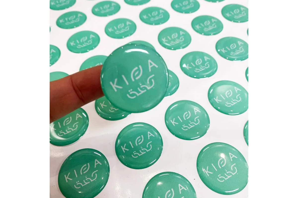 A green round epoxy sample held above a sheet of matching printed labels.
