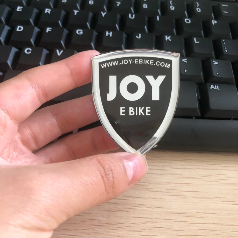 A shield shaped black and silver epoxy badge held in a hand.