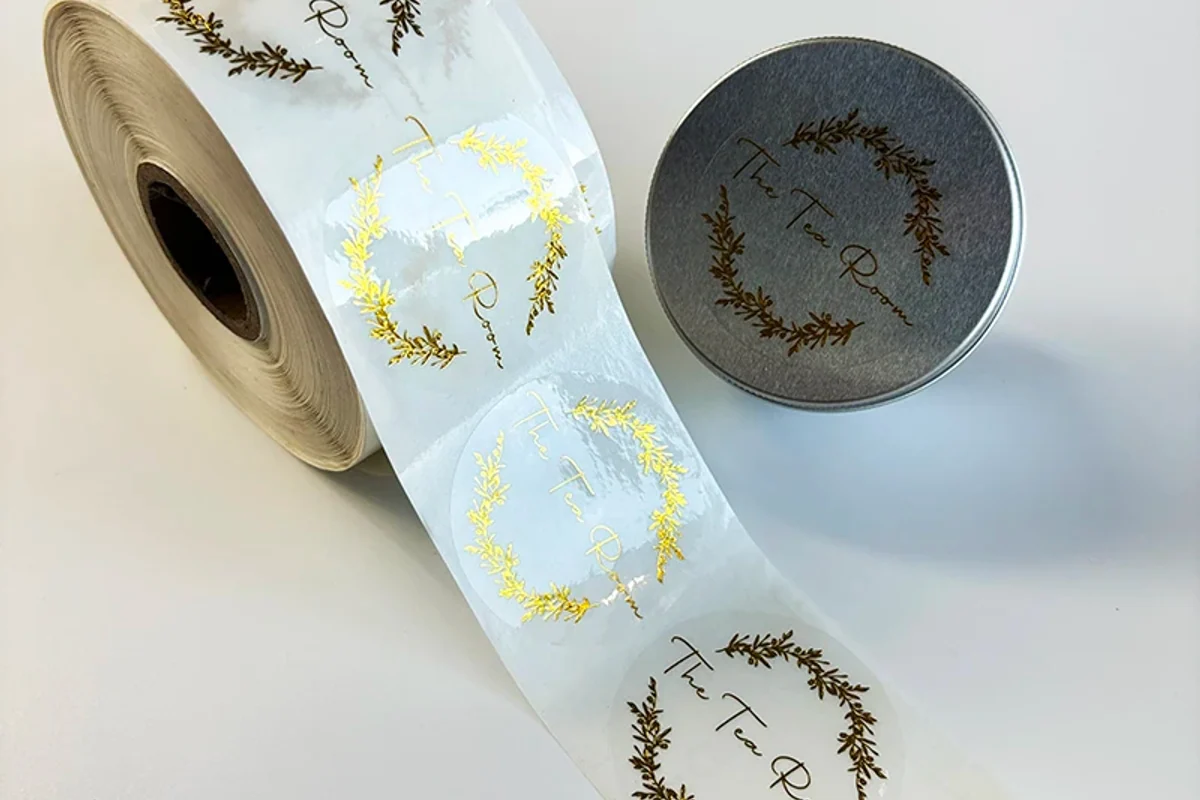 Gold foil logo labels on a roll beside a round tin
