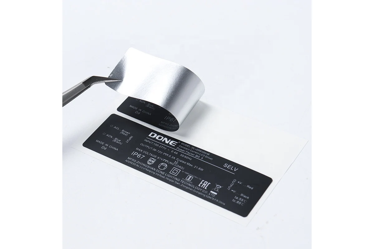 Tweezers lift the silver-backed corner of a black printed equipment label