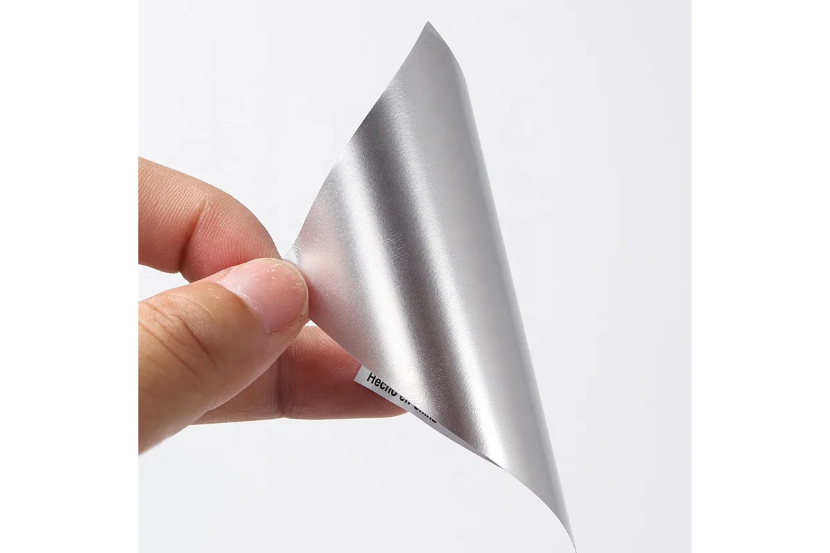 A flexible silver label material sample curled between fingers.