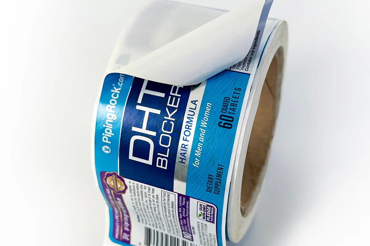 A rectangular label lifted to show its backing on the roll