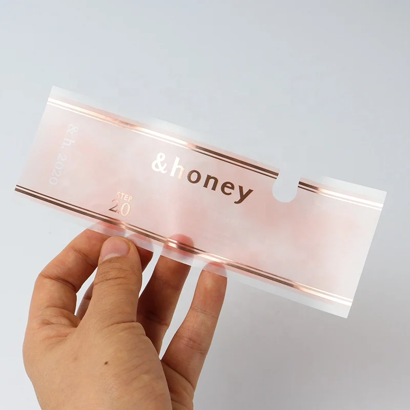 A hand holding a transparent label with pale pink printing.