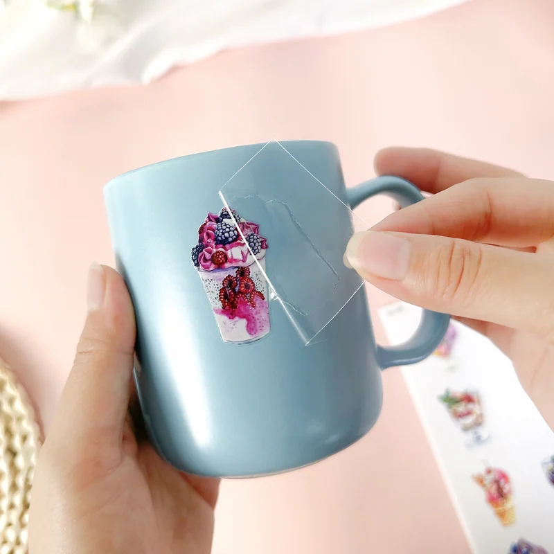 Clear transfer film being lifted from a colorful berry drink illustration on a blue cup.