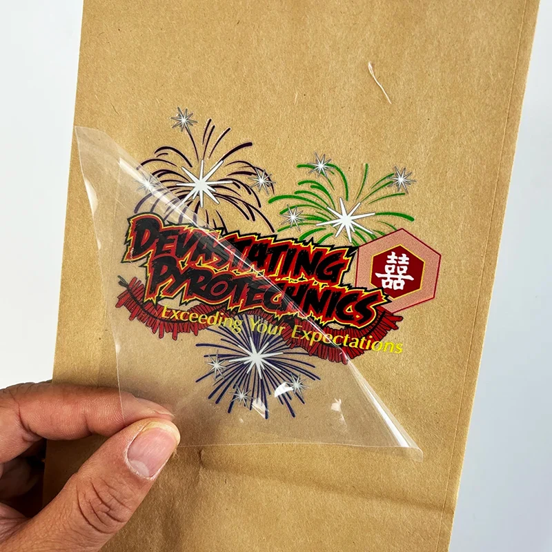 A hand lifting clear carrier film from a single colorful printed transfer on a kraft surface.