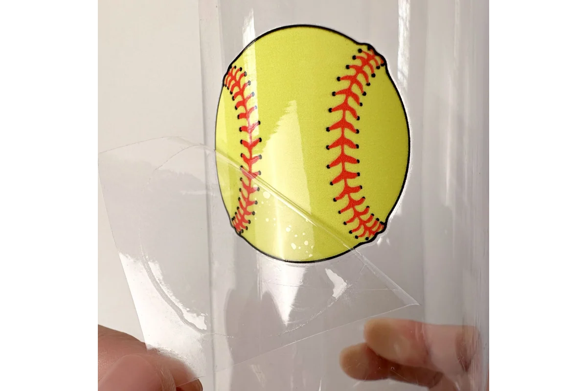 A clear transfer carrier being lifted from a yellow baseball design.
