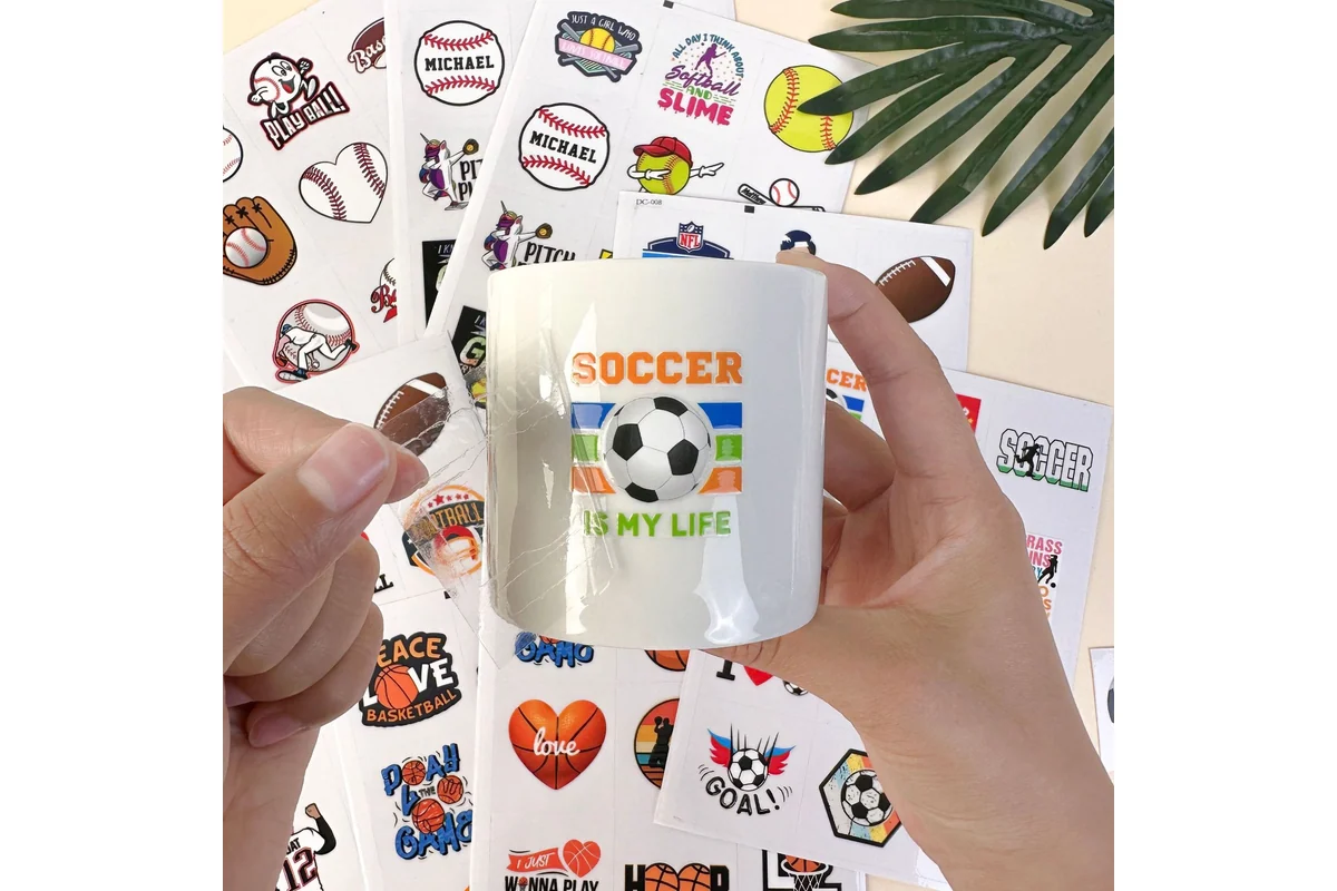 Hands applying a colorful soccer design to a white ceramic mug using clear transfer film.