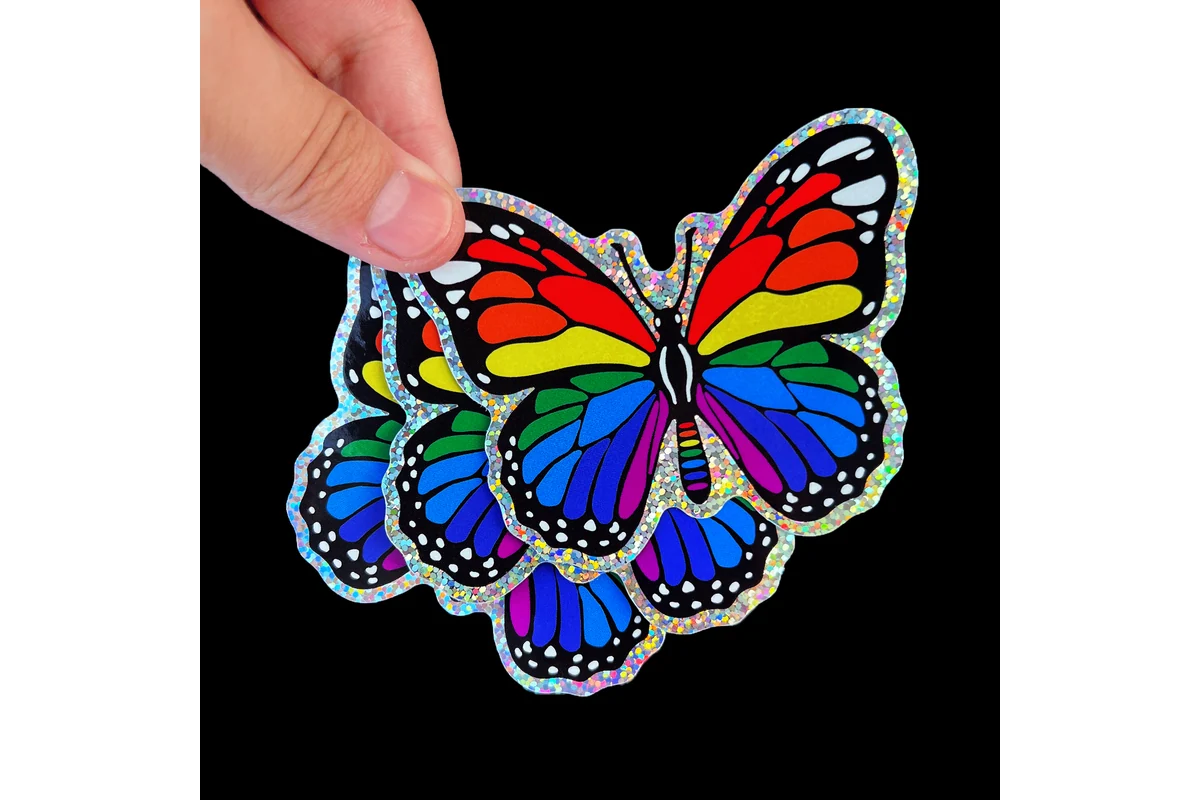 A hand holding butterfly stickers with rainbow colors and a reflective border.