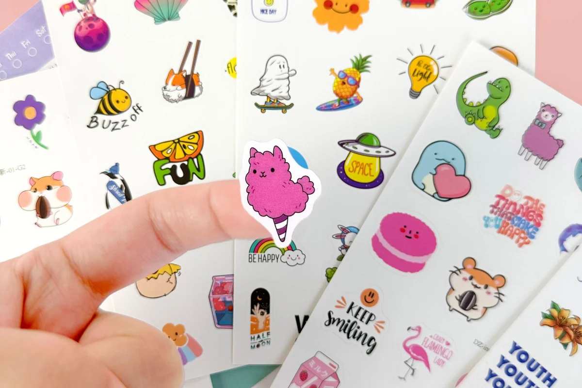 A hand peeling a small printed sticker from a sheet.